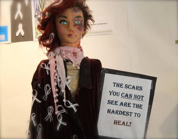 doll with bruises holding sign